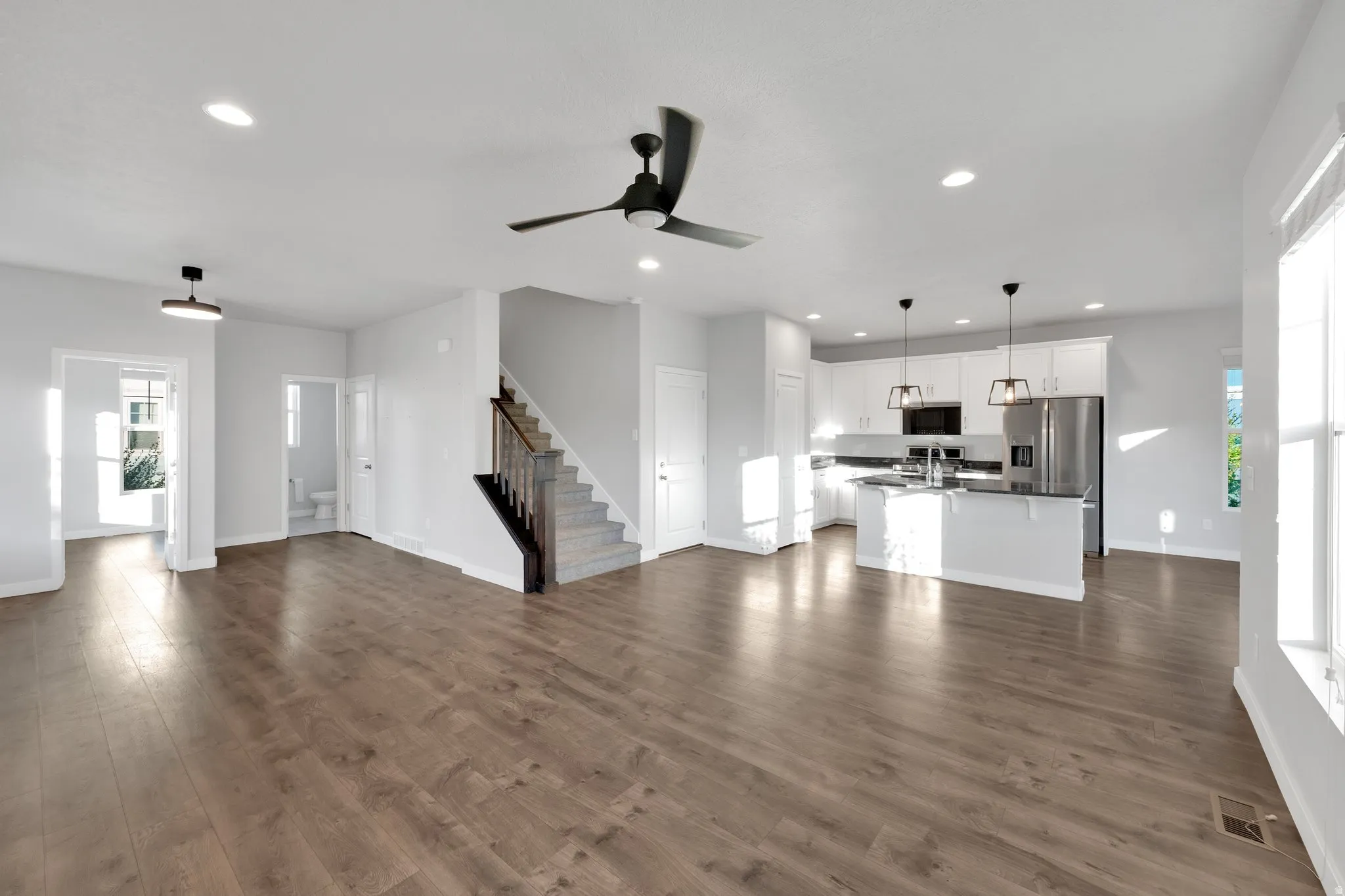 Spacious open-concept living area featuring wood-finish flooring, recessed lighting, and a contemporary ceiling fan