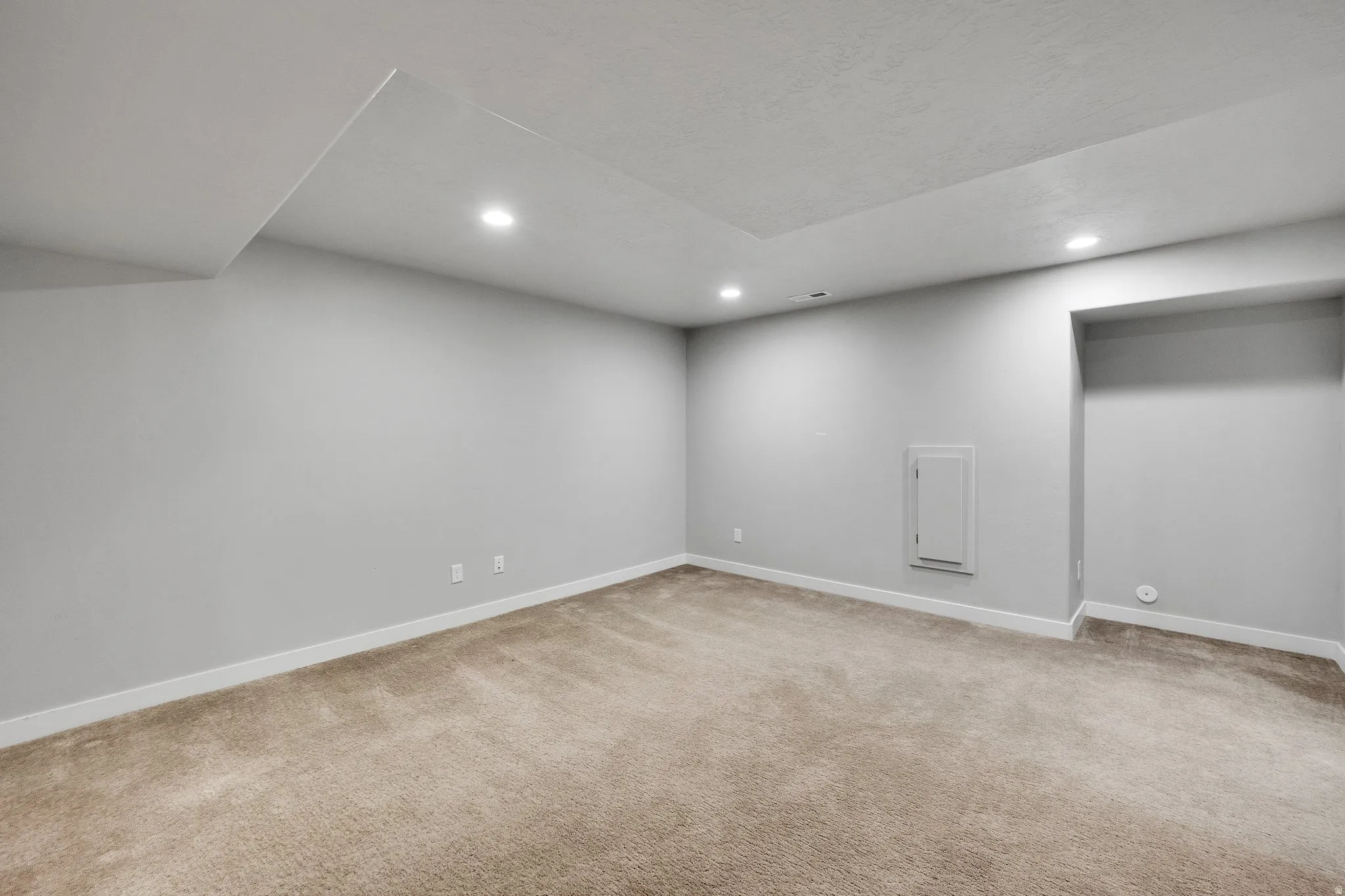 Spacious room featuring neutral carpeting, light-toned wall paint, recessed lighting, white baseboards, and a ceiling with varied heights
