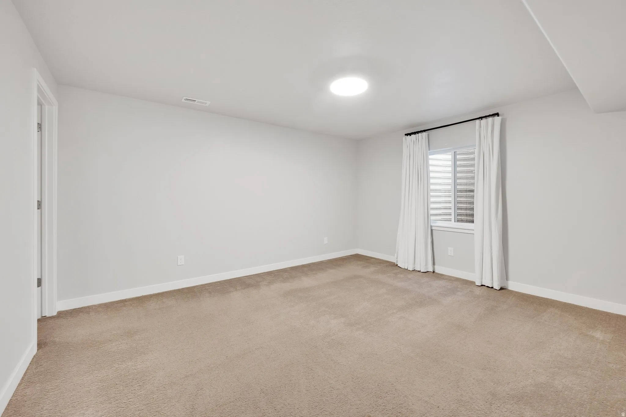 Carpeted interior space with a window featuring horizontal blinds and white drapes