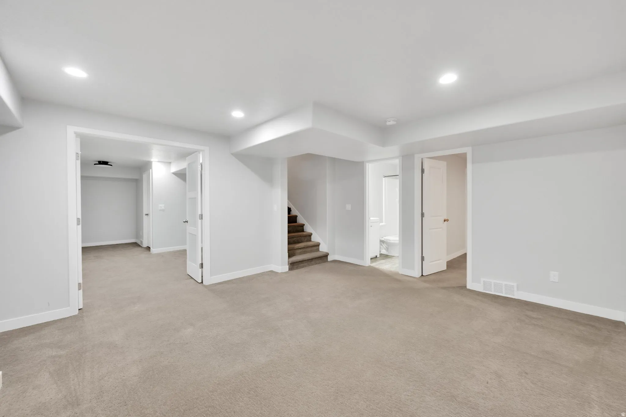 Spacious carpeted area featuring recessed lighting, a staircase with carpeted treads, and multiple doorways leading to additional rooms