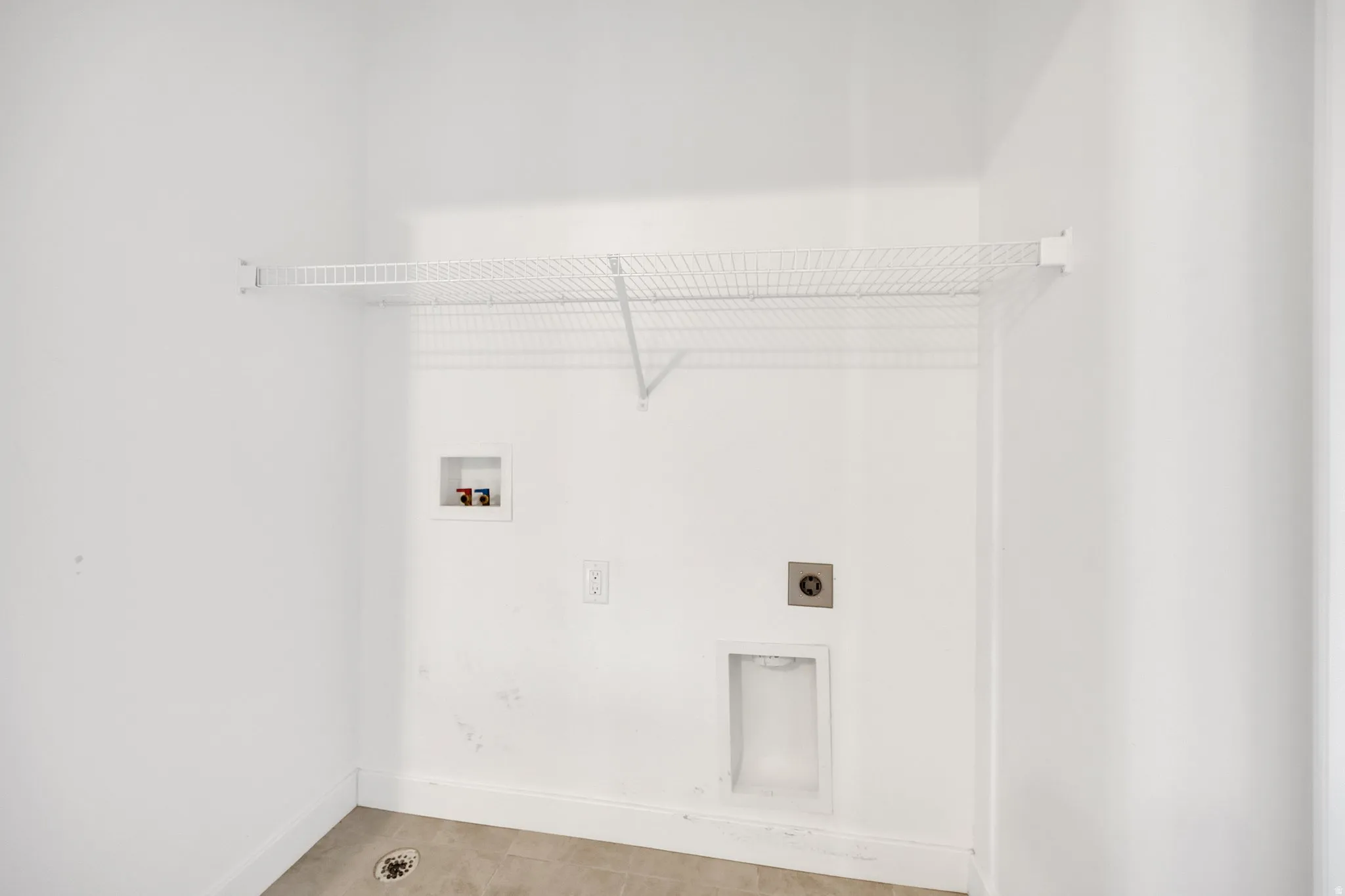 Utility room featuring a wire storage shelf, laundry hookups, and light-toned floor tiling