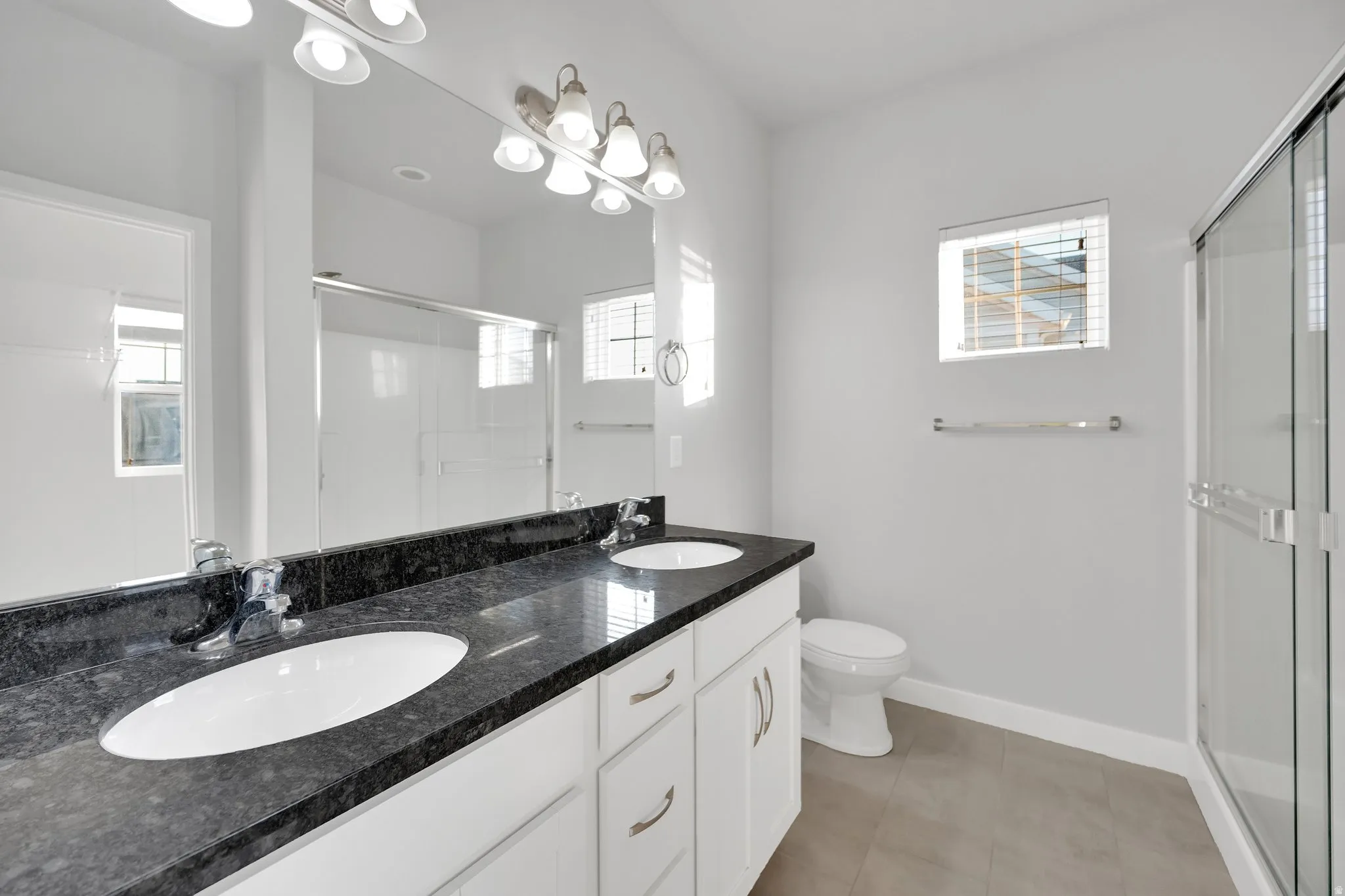 Bathroom featuring a dual vanity with a dark stone countertop, white oval undermount sinks, and a full-width mirror