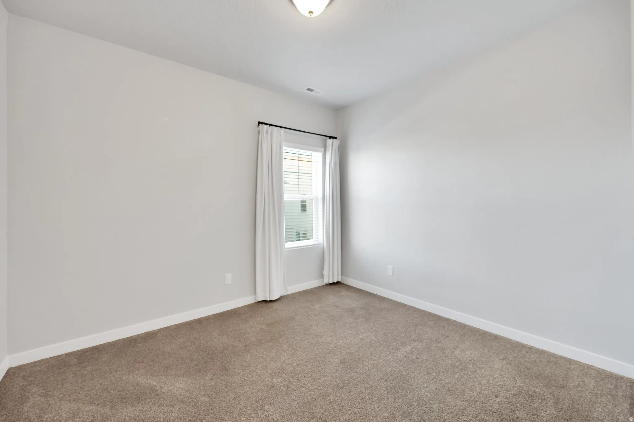 Carpeted room with a single window featuring blinds and white drapery