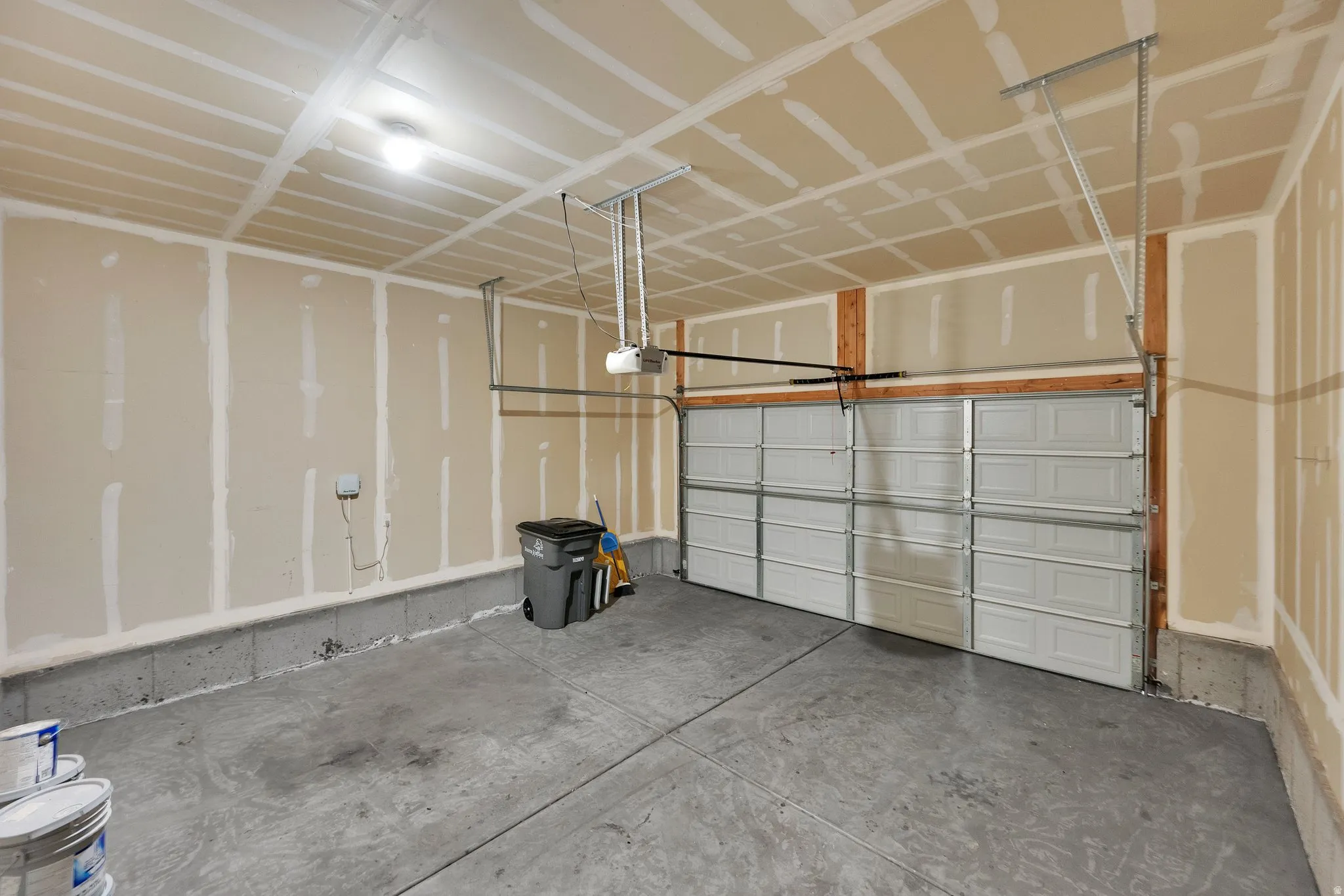 Interior garage featuring a sectioned garage door, concrete flooring, and exposed wood framing elements