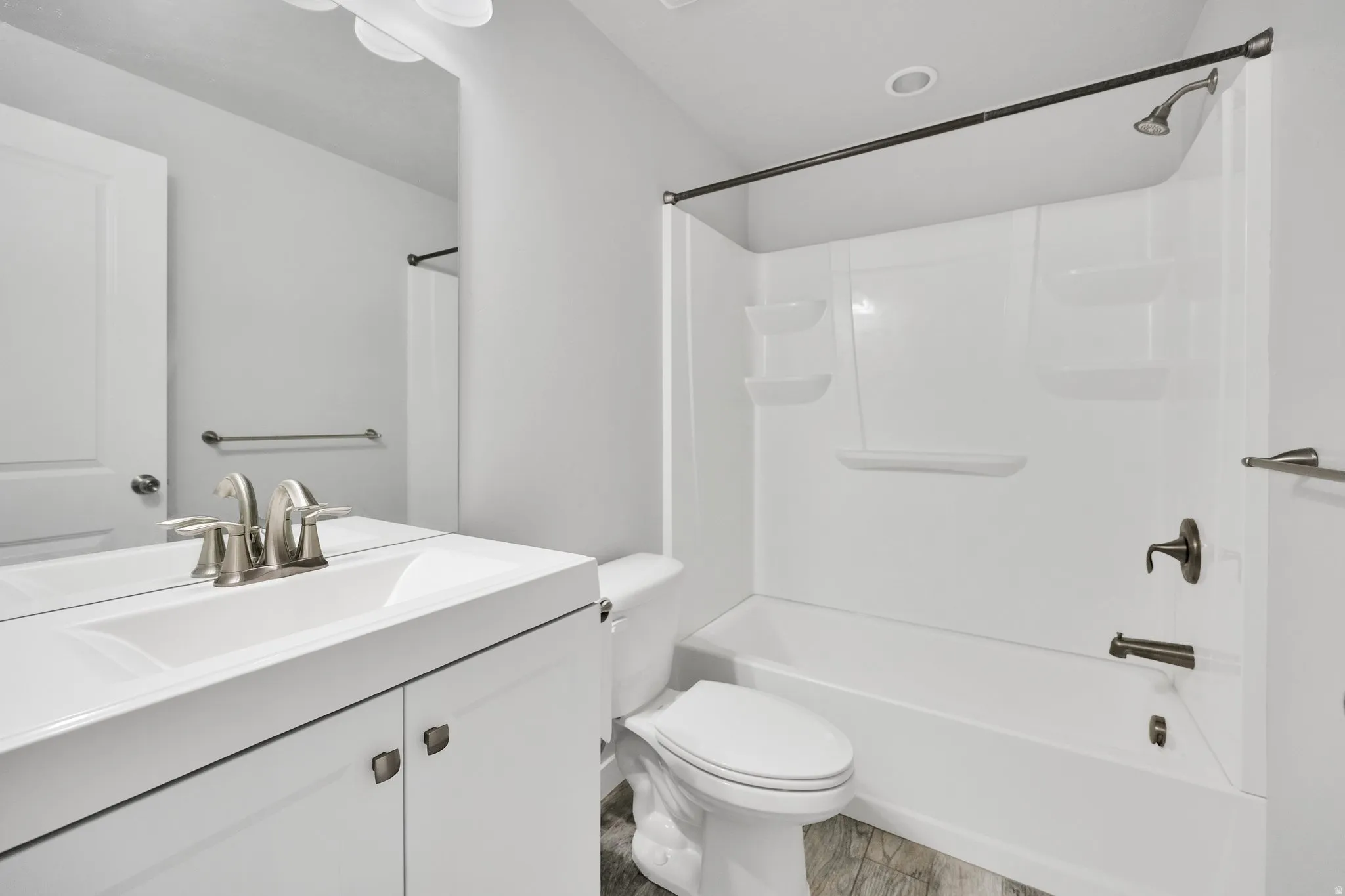 Bathroom featuring a white vanity with integrated sink, brushed nickel faucet, full-width mirror, and a shower-over-tub combination with dark bronze fixtures