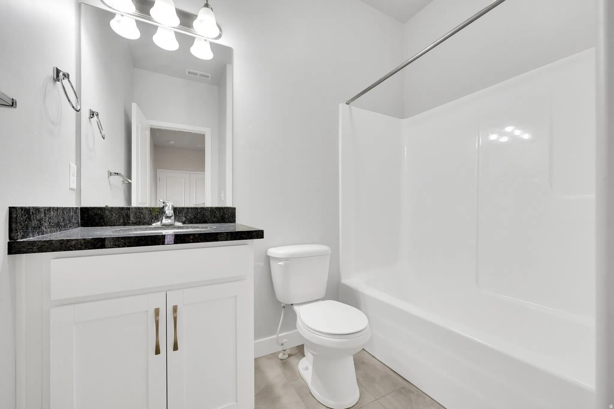 Bathroom featuring a white vanity with bronze hardware, a dark countertop, a mirror, and a white shower/tub combination