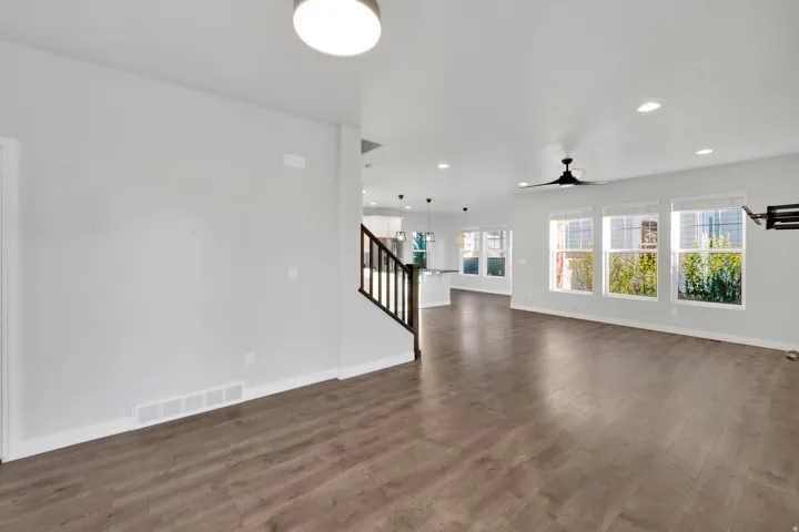 Spacious living area featuring wood-finish flooring, ample natural light from multiple windows, and a contemporary ceiling fan