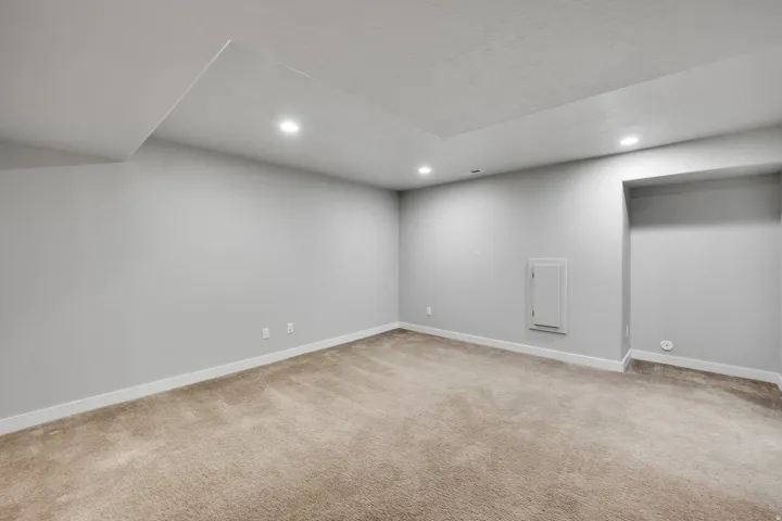 Spacious room featuring neutral carpeting, light-toned wall paint, recessed lighting, white baseboards, and a ceiling with varied heights