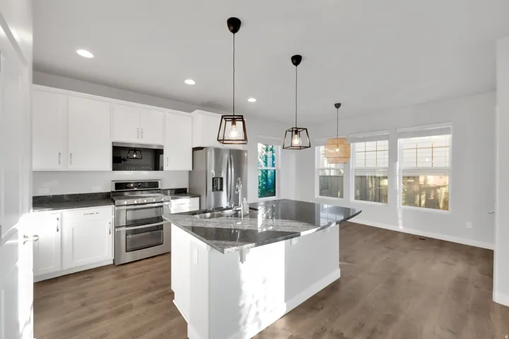 Contemporary kitchen featuring white cabinetry, stainless steel appliances, dark stone countertops, a central island with an undermount sink, and wood-finish flooring