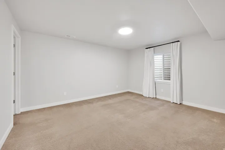 Carpeted interior space with a window featuring horizontal blinds and white drapes