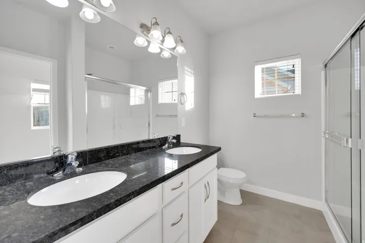 Bathroom featuring a dual vanity with a dark stone countertop, white oval undermount sinks, and a full-width mirror