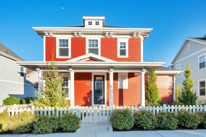 Red two-story residence featuring white trim, a covered front porch with columns, a white picket fence, and established front landscaping
