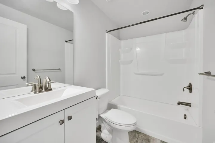 Bathroom featuring a white vanity with integrated sink, brushed nickel faucet, full-width mirror, and a shower-over-tub combination with dark bronze fixtures