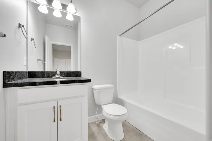 Bathroom featuring a white vanity with bronze hardware, a dark countertop, a mirror, and a white shower/tub combination