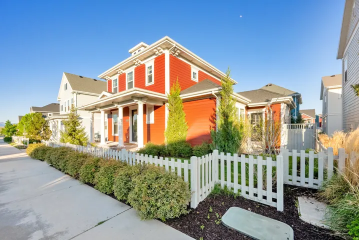 Red exterior with white trim, featuring a columned front porch, multiple windows, and a picket fence