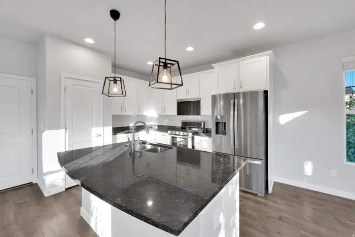 Kitchen island with a dark countertop, stainless steel appliances, white cabinetry, wood-finish flooring, and recessed lighting