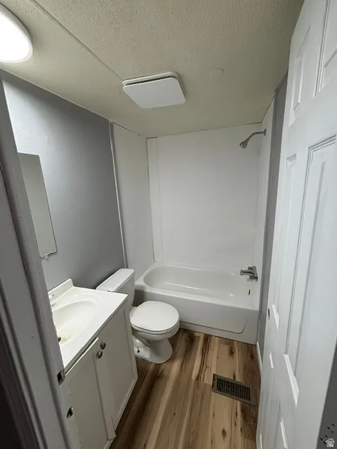 Bathroom featuring a white vanity with integrated sink, wood-finish flooring, a white toilet, and a white tub with shower