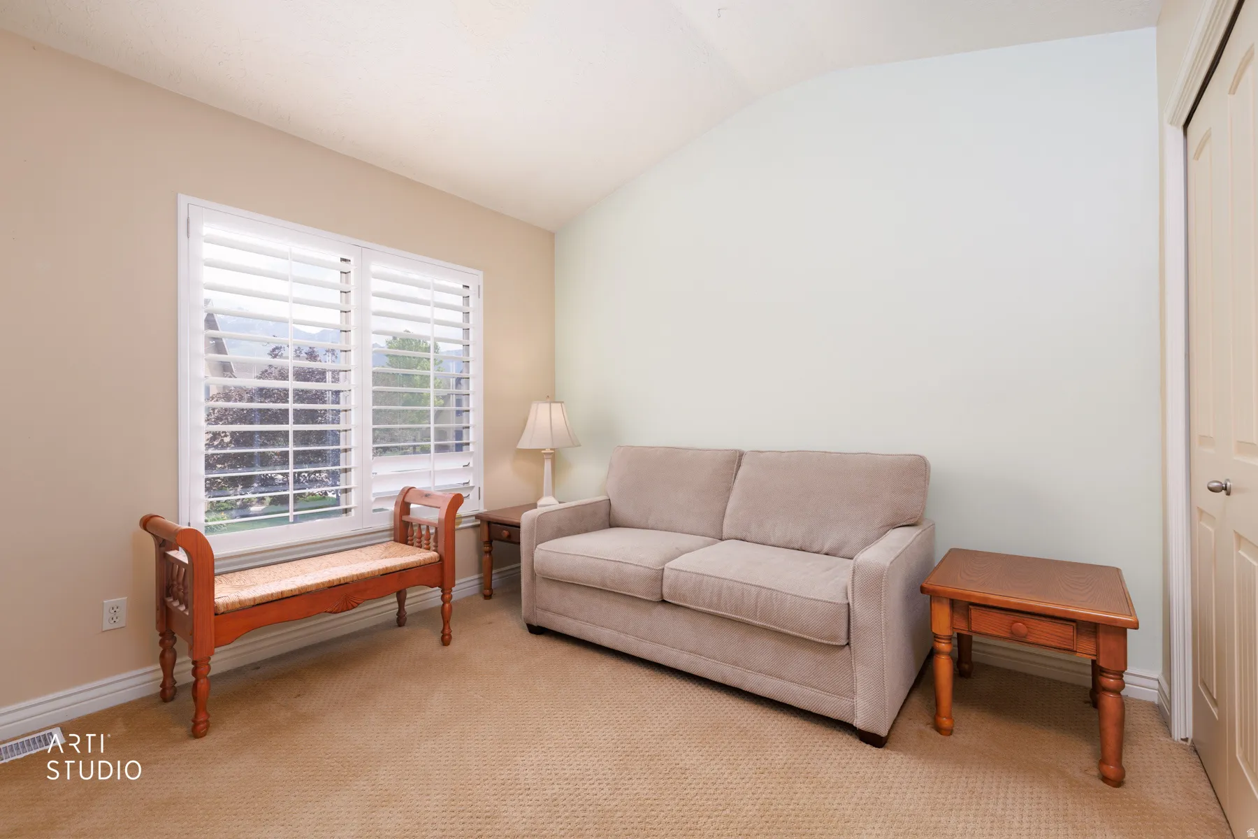 Room featuring a vaulted ceiling and a window with white louvered shutters