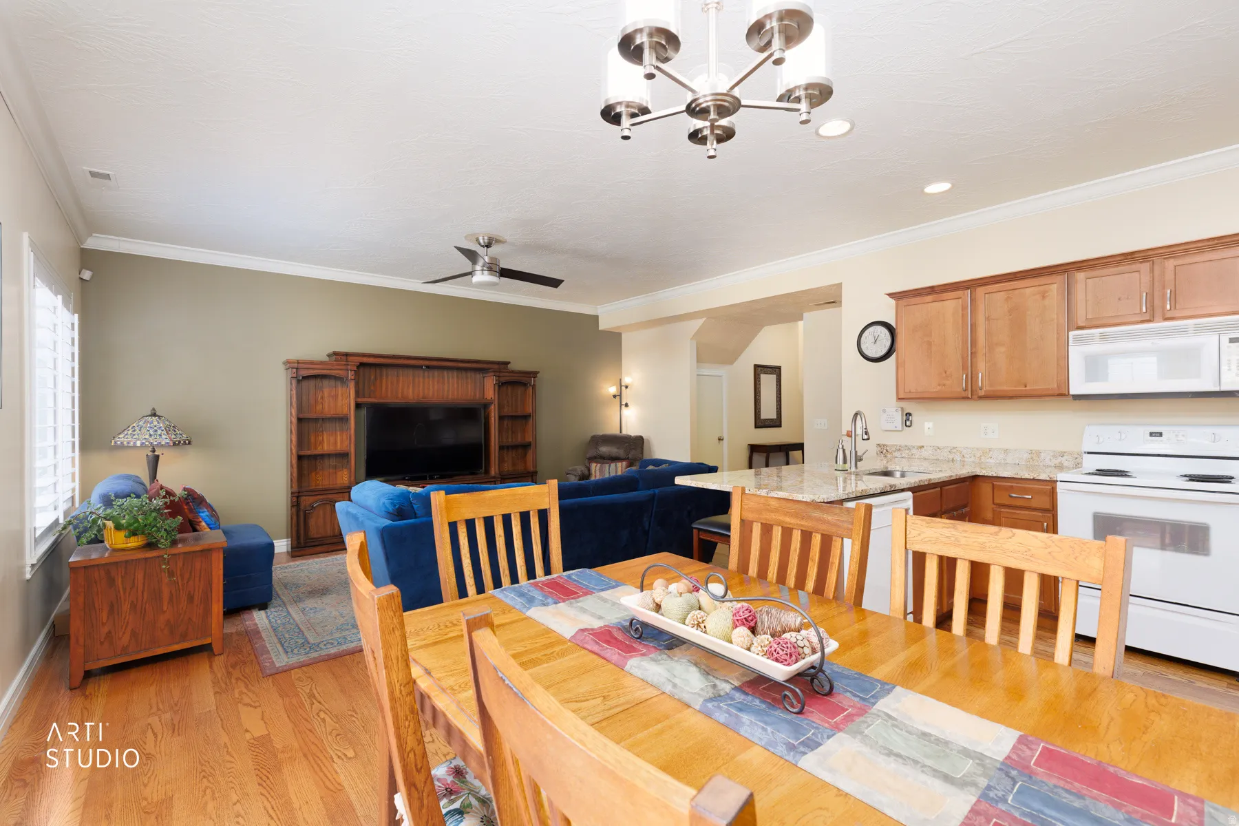 Open-concept living space with wood-finish flooring, a contemporary ceiling fan, and crown molding
