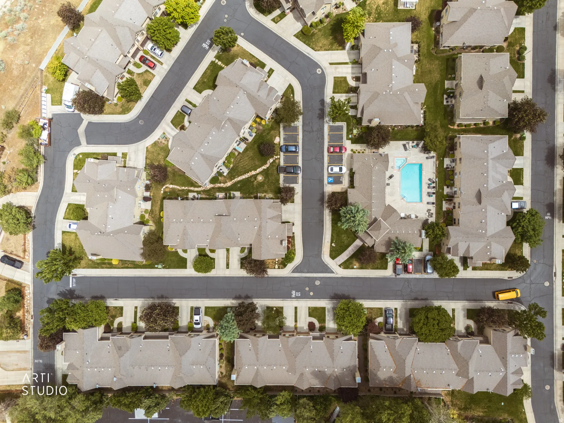 Aerial overview of a residential community featuring multiple buildings with gabled roofs, a central swimming pool with surrounding lounge chairs, and designated parking areas