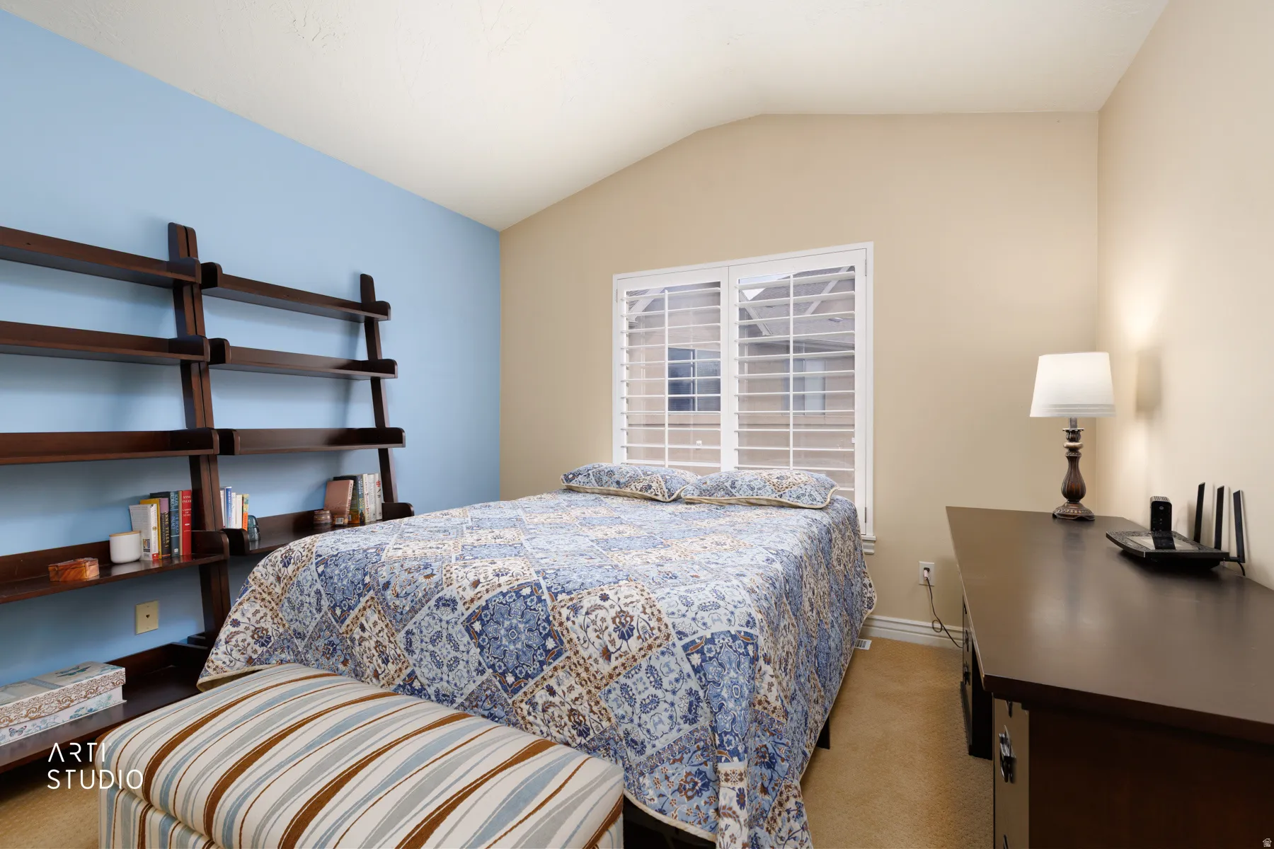 Vaulted ceiling room featuring a large window with white plantation shutters, a built-in wooden ladder-style shelving unit, and warm-toned carpeting