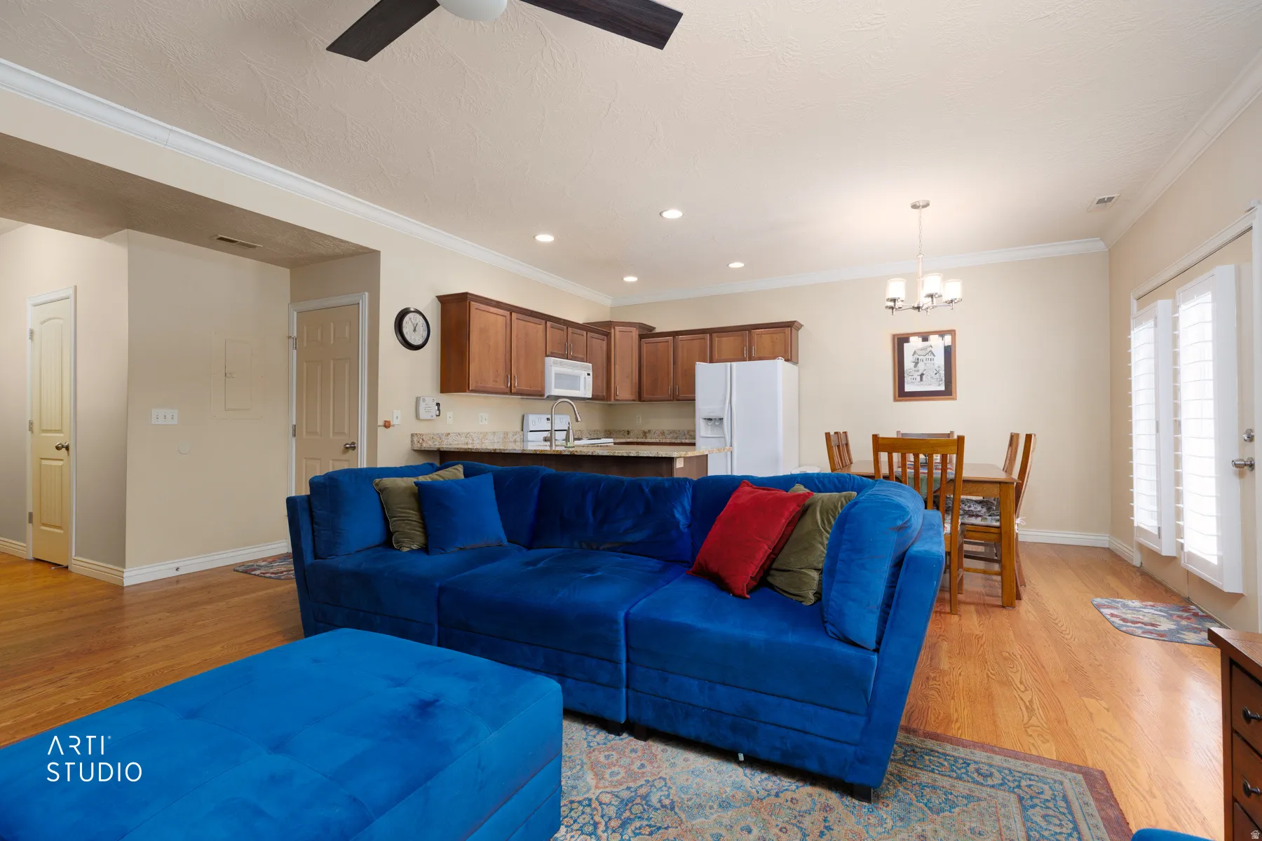 Open-concept living area with wood-finish flooring, crown molding, and a ceiling fan
