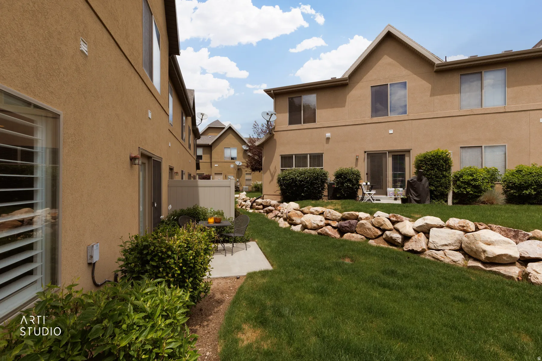 Rear exterior featuring a rock retaining wall, mature landscaping, and a patio with direct access to the interior