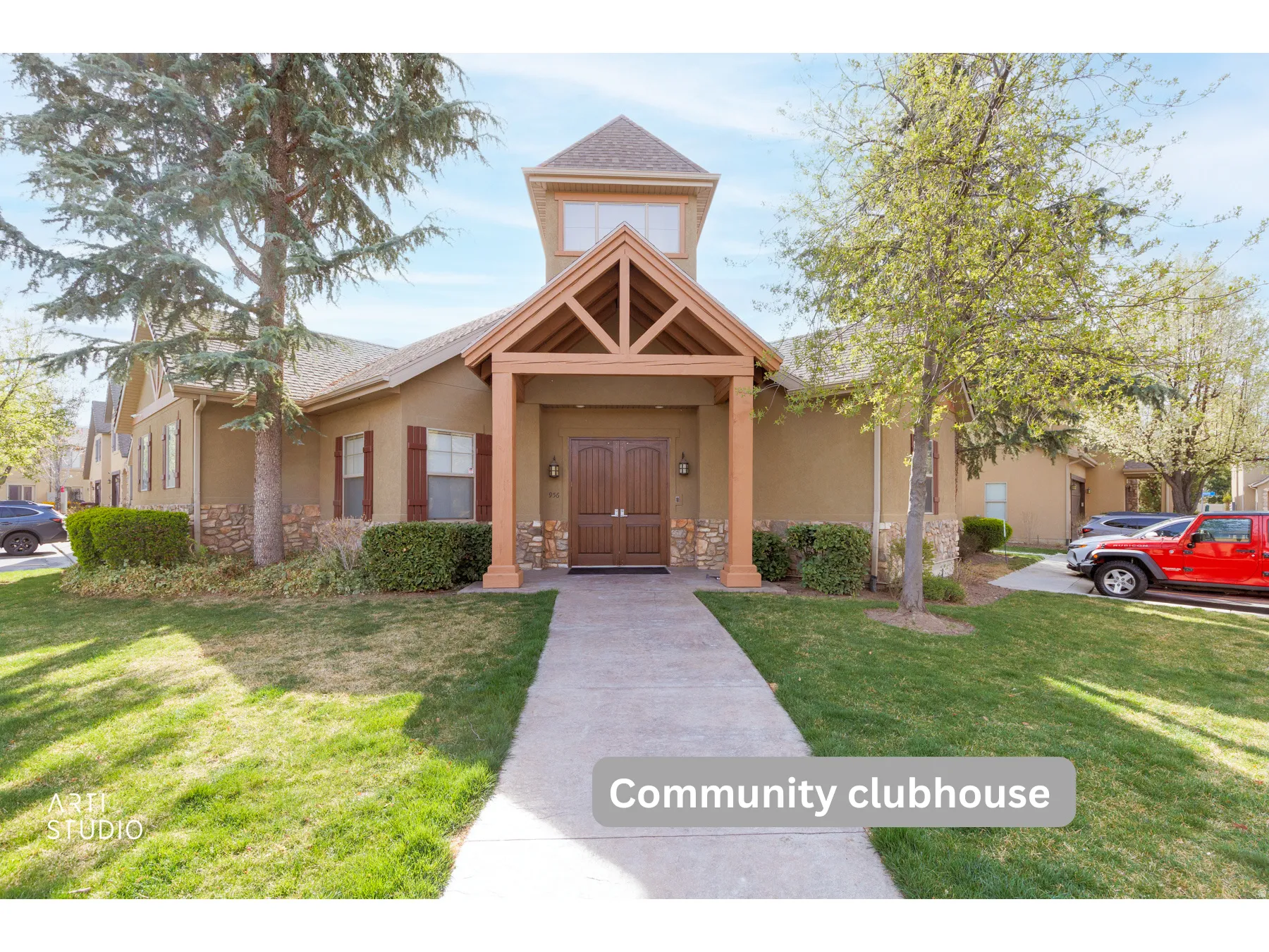 Community clubhouse featuring a stucco exterior, stone base accents, a prominent covered entry with exposed wood beams, and a central tower with upper-level windows