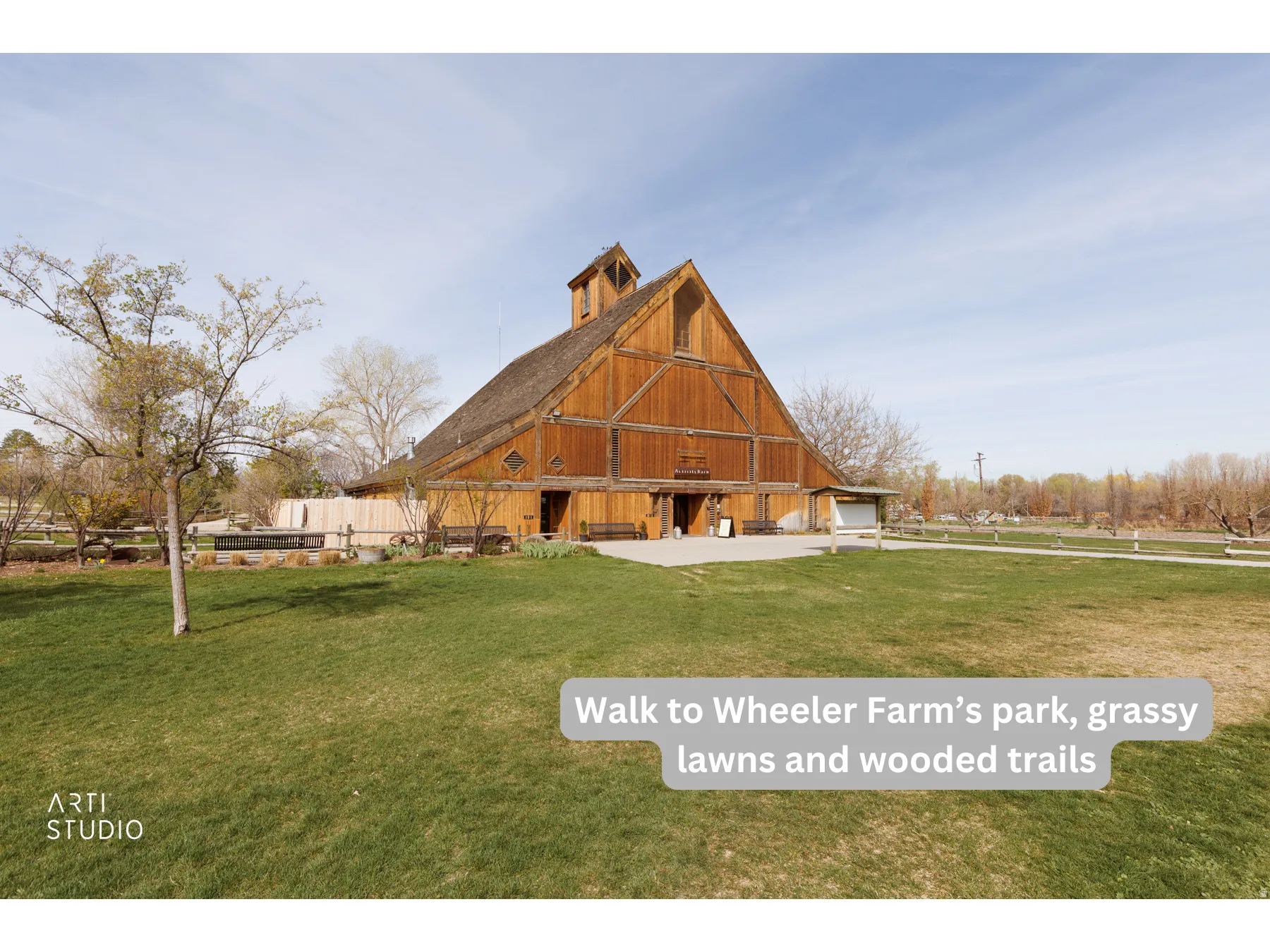 Expansive green space featuring a large wooden barn structure with a prominent gabled roof and cupola, surrounded by mature trees and a fenced perimeter