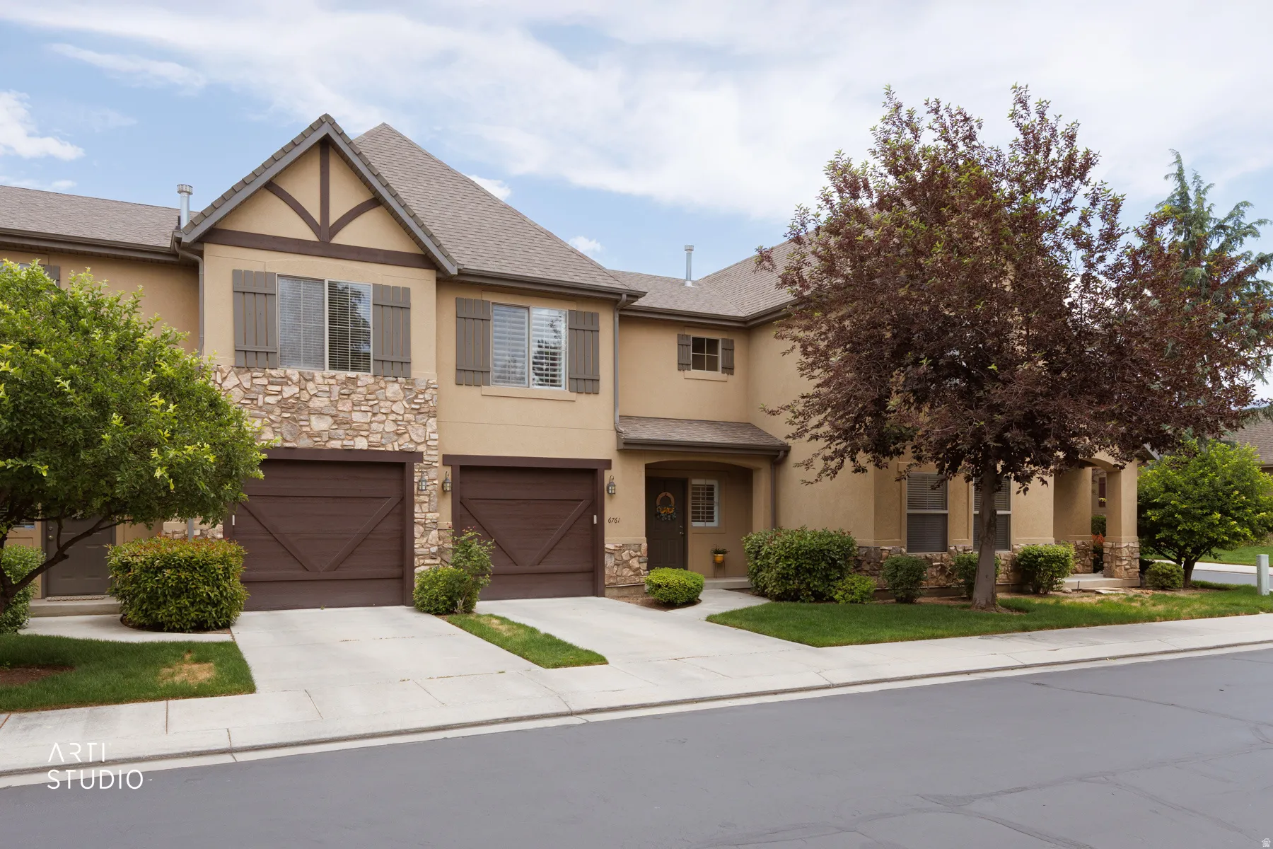 Stucco and stone facade featuring decorative gable accents, two single-car garage doors with carriage house styling, and mature landscaping