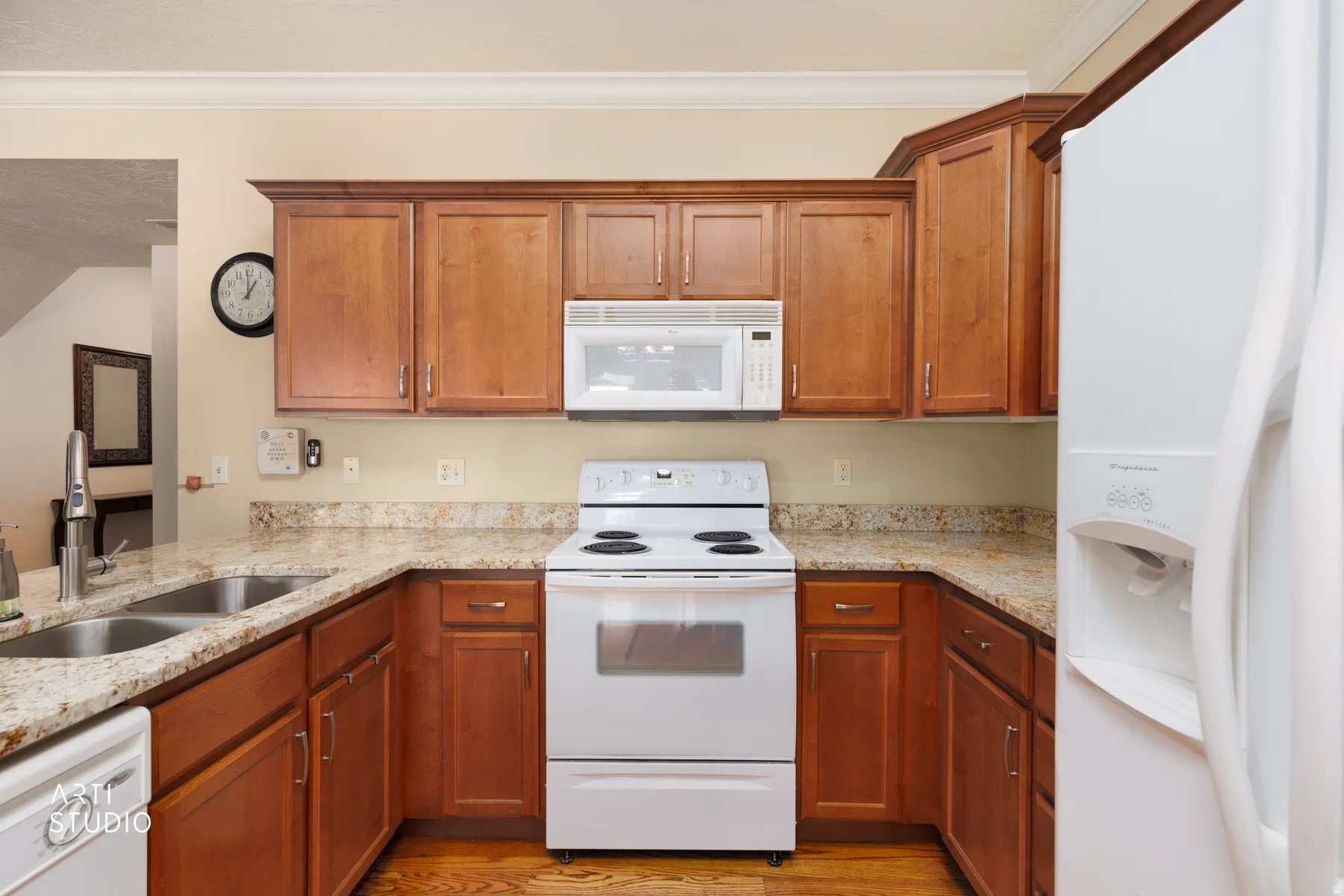 Kitchen featuring wood cabinetry, light-toned countertops, a double basin sink with a high-arc faucet, white appliances, and wood-finish flooring