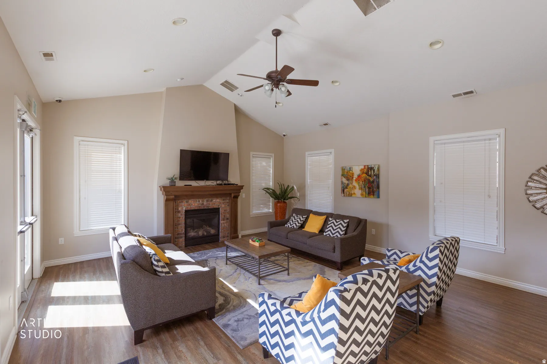 Community Clubhouse - Vaulted ceiling great room featuring a prominent fireplace with a wood mantle, wood-finish flooring, recessed lighting, and a ceiling fan