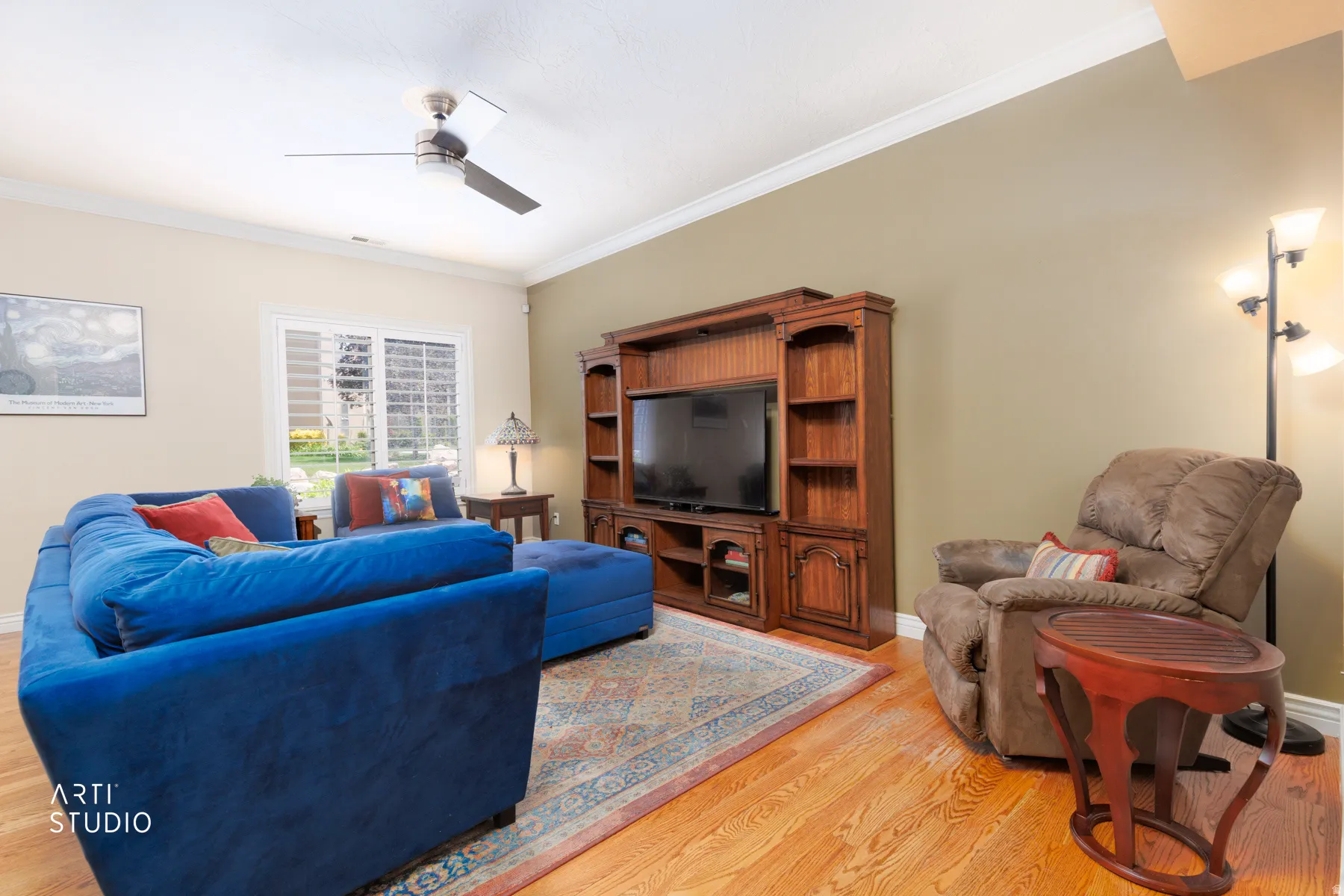 Living area featuring wood-finish flooring, a wood entertainment center with built-in shelving, and a ceiling fan
