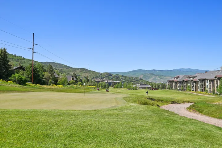 Expansive green golf course with a flagstick, bordered by residential structures and distant mountains