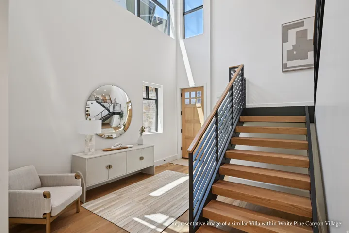 Two-story foyer with high ceilings, large windows, wood-finish flooring, a wood entry door, and a staircase featuring wood treads and a metal railing