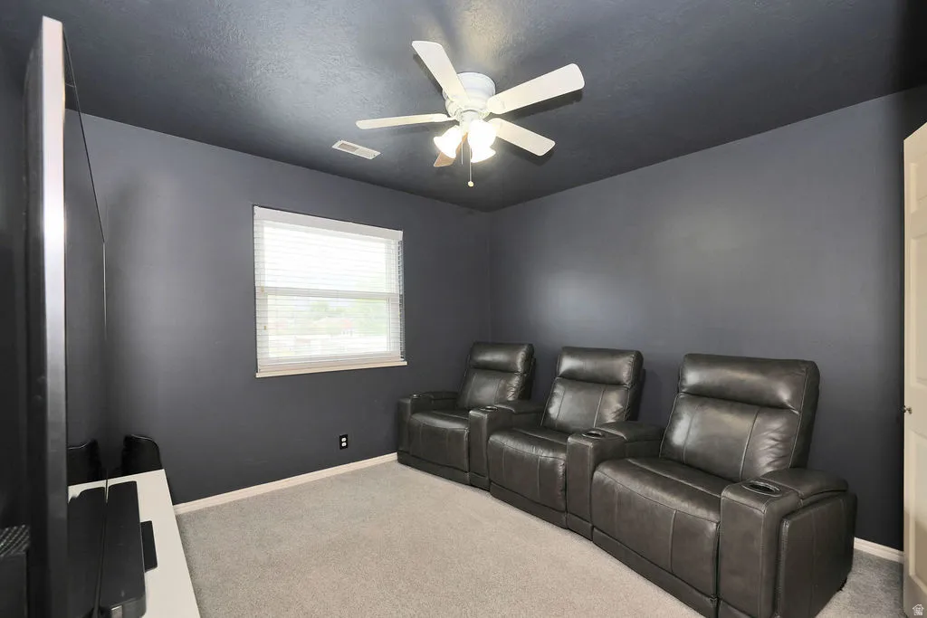 Media room featuring dark-painted walls and ceiling, a ceiling fan, a window with blinds, and light-colored carpeting