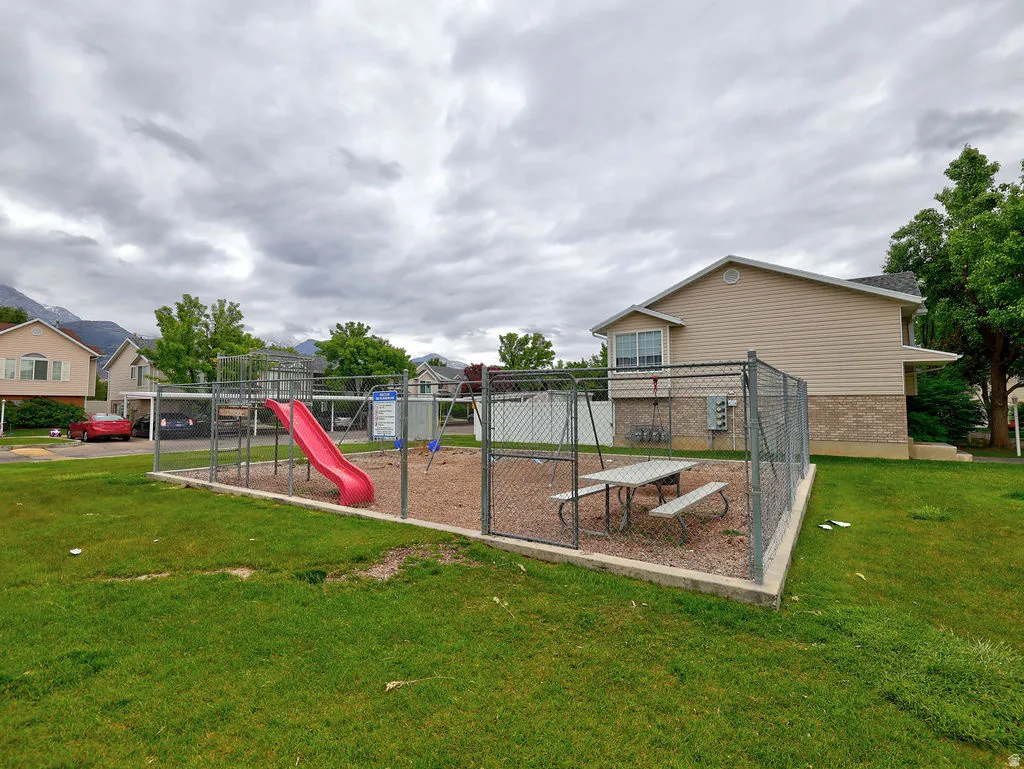 Fenced playground area featuring a red slide, swing set, and picnic table