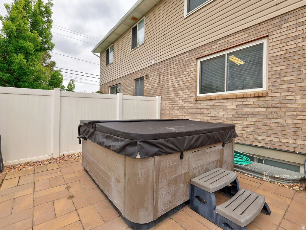 Patio area featuring a spa with a protective cover, flanked by a white privacy fence