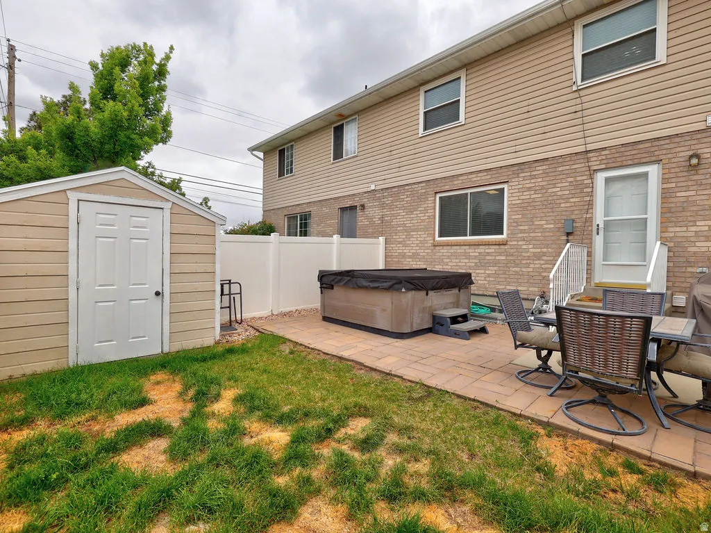 Backyard featuring a paver patio, a hot tub with cover, and a storage shed