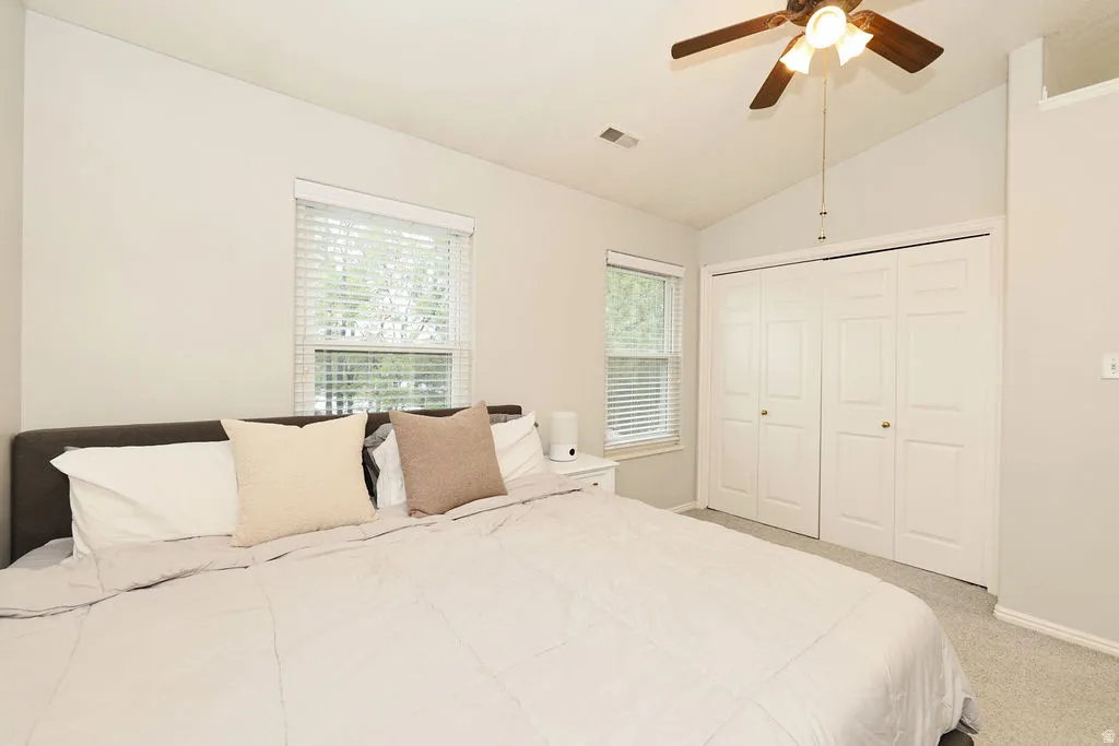 Bedroom featuring vaulted ceilings, ceiling fan, carpet flooring, windows with blinds, and bi-fold closet doors