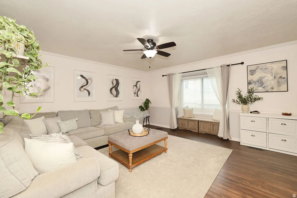 Spacious living area featuring wood-finish flooring, a ceiling fan with integrated lighting, and a window with blinds and drapes