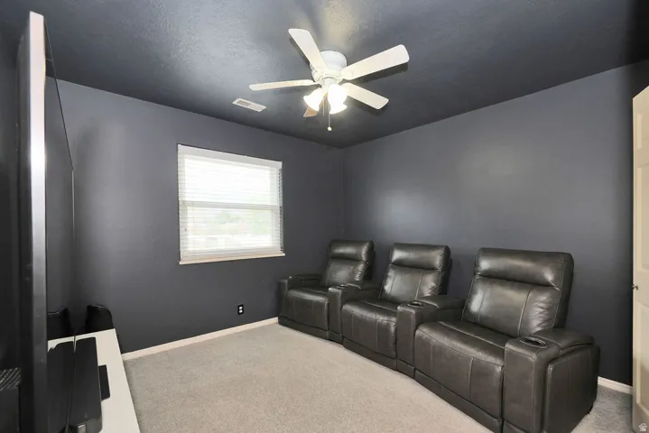 Media room featuring dark-painted walls and ceiling, a ceiling fan, a window with blinds, and light-colored carpeting