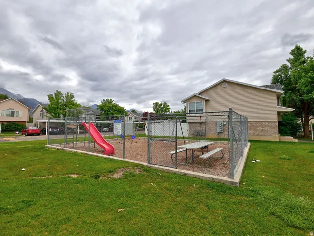 Fenced playground area featuring a red slide, swing set, and picnic table