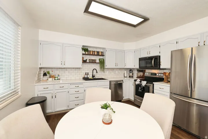 Bright kitchen with white cabinetry, stainless steel appliances, a subway tile backsplash, wood-finish flooring, and a large recessed ceiling light fixture
