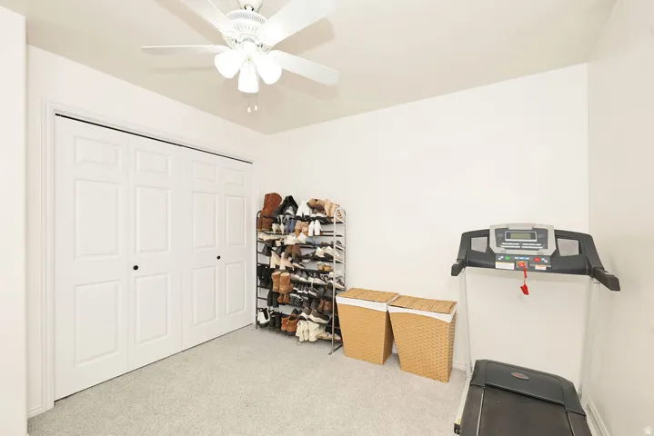 White paneled bi-fold closet doors, light-colored carpeting, and a ceiling fan with light fixture