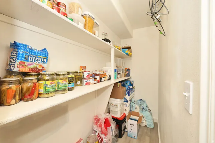 Spacious pantry with multiple levels of built-in shelving, light-toned walls, and wood-finish flooring