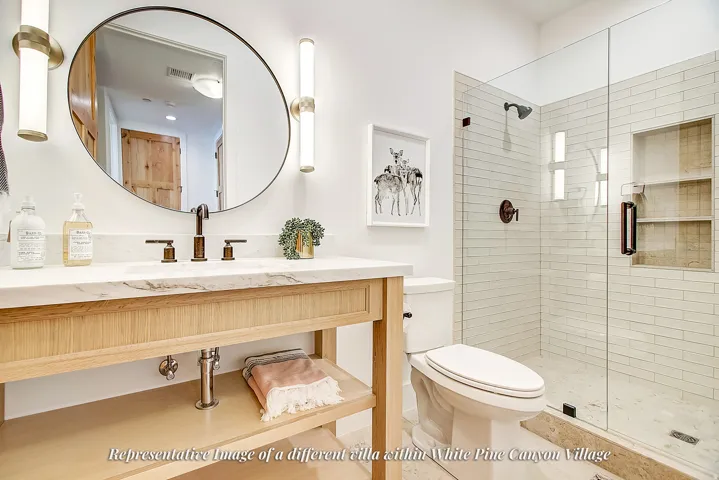 Bathroom featuring a wood-finish vanity with a stone countertop, a circular mirror, and a glass-enclosed shower with subway tile