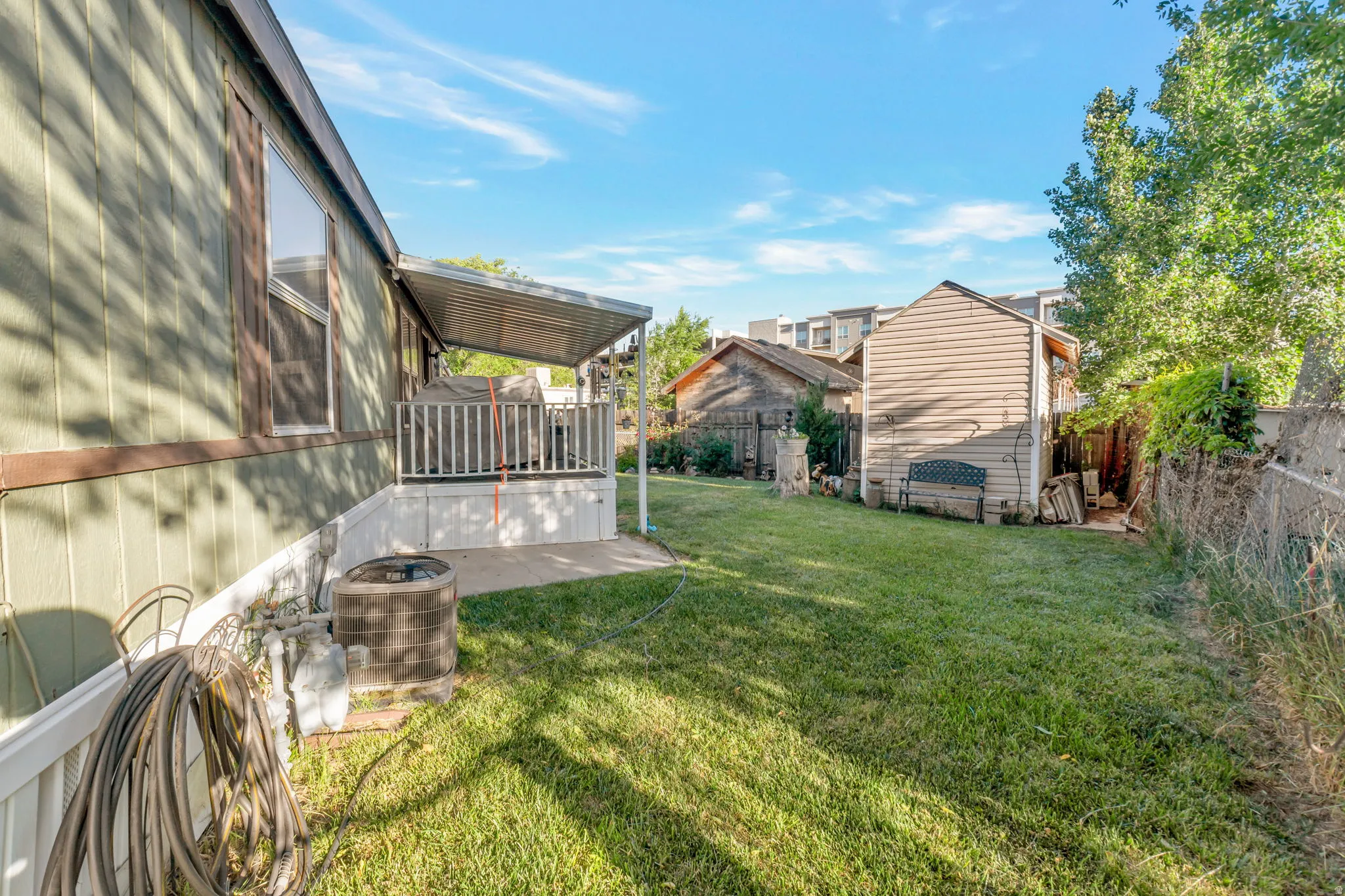 Spacious grassy yard featuring a covered patio with railing, a detached storage shed, and mature perimeter trees