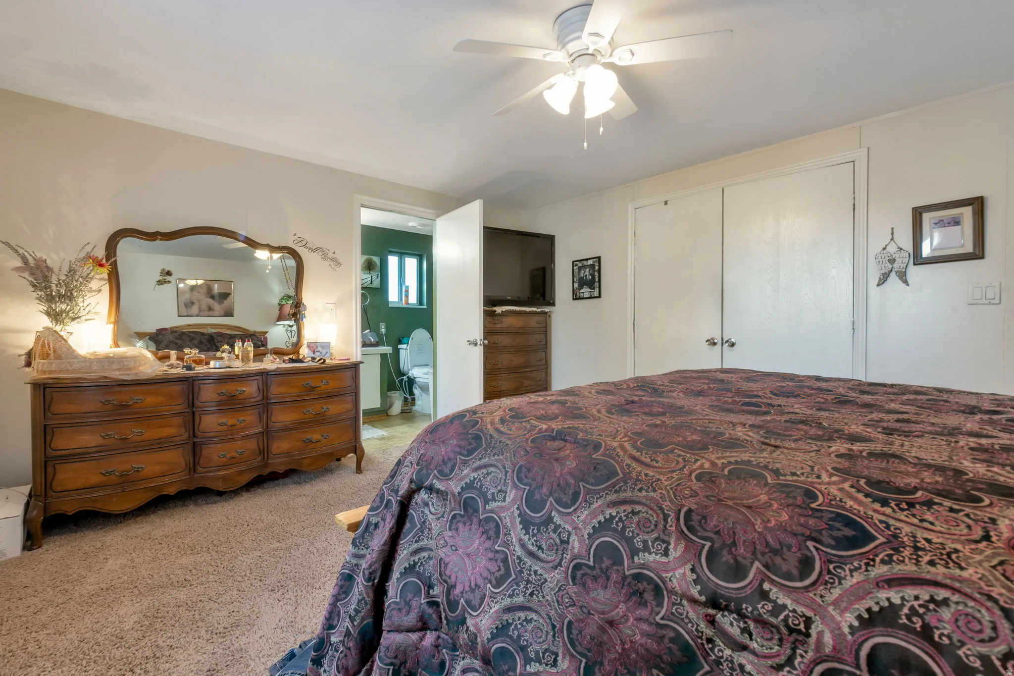 Carpeted bedroom featuring a ceiling fan with integrated lighting, two bi-fold closet doors, and access to an adjoining bathroom
