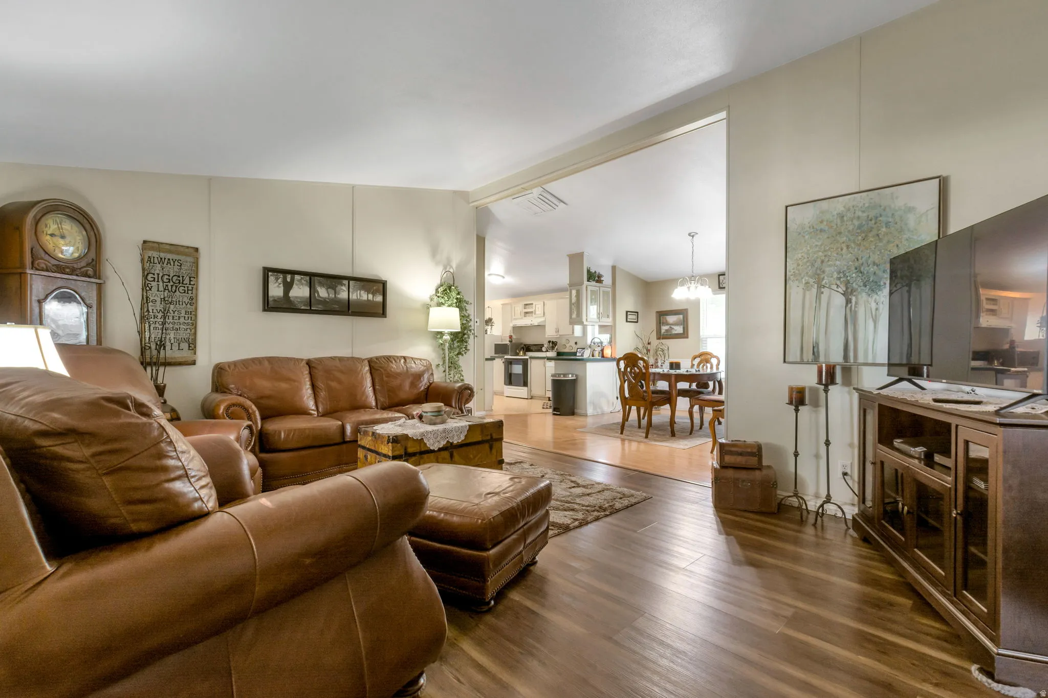 Spacious living area featuring wood-finish flooring, light-colored walls, and an open architectural design that reveals the kitchen and dining areas